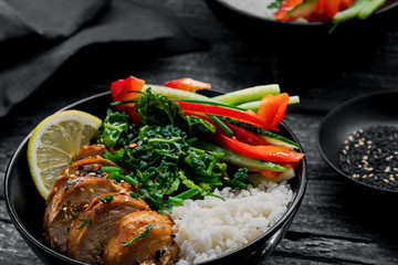 Wall Mural - Two lunch bowls with teriyaki chicken, cucumber, red bell pepper, green onion, stew spinach and basmati rice on a rustic black table.