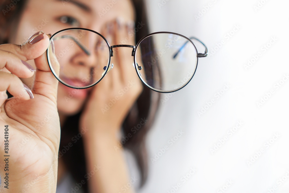 Asian woman hand holding eyeglasses having problem with eye pain, blur vision  - obrazy, fototapety, plakaty 