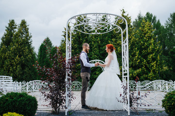 Wall Mural - Newly wed couple standing under white metal arches in a park, holding hands