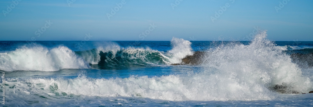 Large ocean waves crash against coastal stones on sunny day on European coast. Holidays, vacations on Atlantic ocean. High waves, surfing in Europe. Panoramic view. Tidal bore. Bay of Biscay, Spain. - obrazy, fototapety, plakaty 