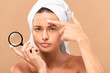 displeased girl pointing with finger at pimple on face and holding magnifier isolated on beige