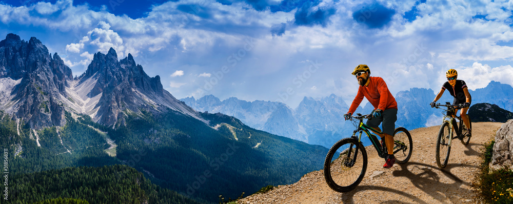 Cycling woman and man riding on bikes in Dolomites mountains andscape. Couple cycling MTB enduro trail track. Outdoor sport activity. - obrazy, fototapety, plakaty 
