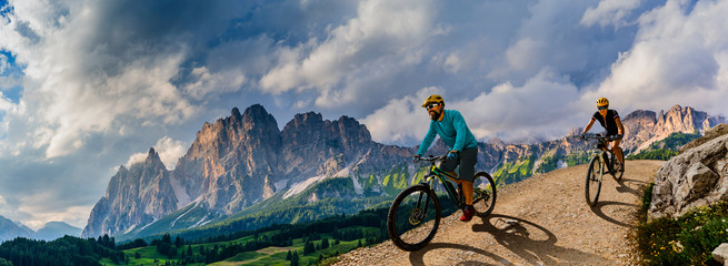 Cycling woman and man riding on bikes in Dolomites mountains andscape. Couple cycling MTB enduro trail track. Outdoor sport activity.