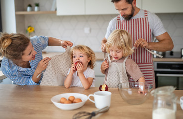 Young family with two small children indoors in kitchen, cooking.