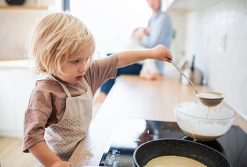 A small boy helping indoors in kitchen with making pancakes.