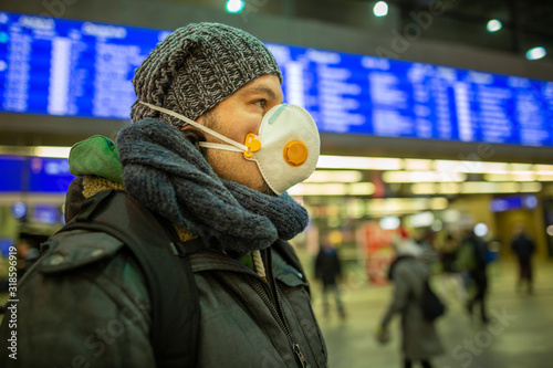 Cuadros en Lienzo Man wearing a respirator mask device for health protection at an airport or railway train station in a crowd of people while travelling
