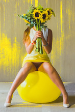 Woman Holding Sunflowers While Sitting On Yellow Fitness Ball