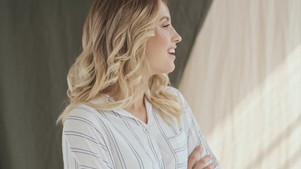 Sticker - An attractive elegant blonde woman is smiling and standing with arms crossed in studio over fabric background