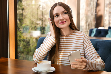 Canvas Print - Woman listening to audiobook at table in cafe