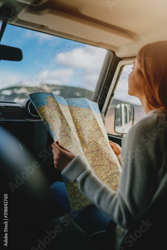 Vertical image of young traveler girl sitting in vintage car exploring map, beautiful woman with long hair traveling by car searching new direction, vintage lifestyle traveling, sunny weather