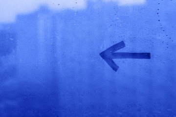 Hand drawn one arrow pointing to the left on foggy glass of blue window, concept photo, copy space