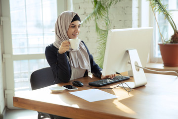 Wall Mural - Working online. Portrait of a beautiful arabian businesswoman wearing hijab while working at openspace or office. Concept of occupation, freedom in business area, leadership, success, modern solution.