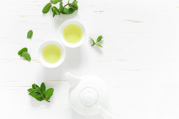 Wall Mural - Green mint tea with fresh leaves in cups and teapot overhead on white wooden table, healthy warming drink, antioxidant beverage, top view