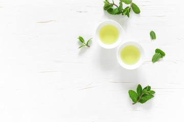 Wall Mural - Green mint tea with fresh leaves in cups and teapot overhead on white wooden table, healthy warming drink, antioxidant beverage, top view