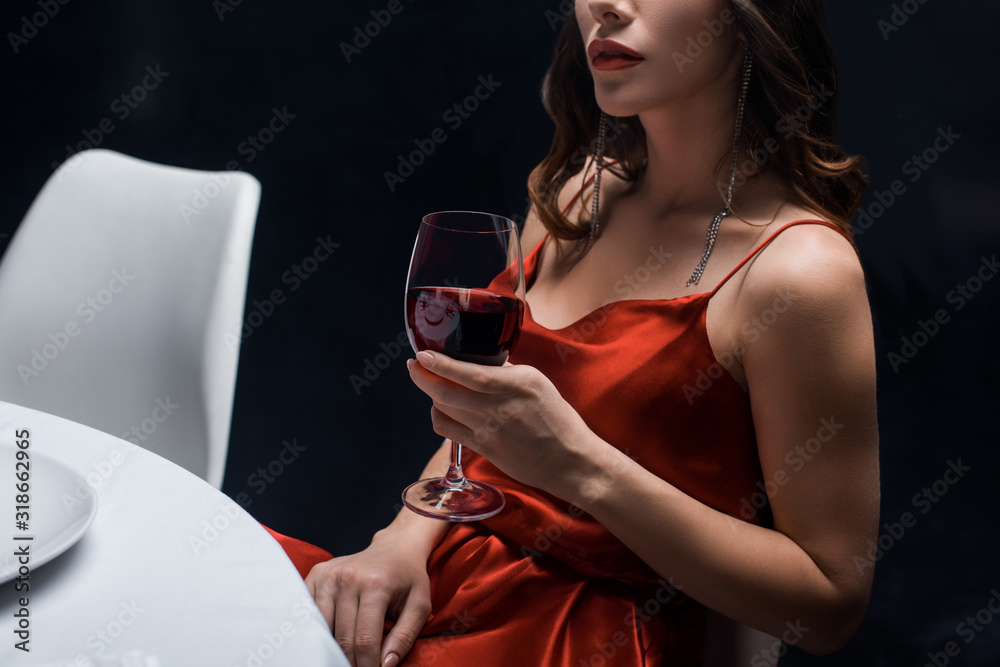 Cropped view of elegant woman in red dress holding wine glass at table  isolated on black Stock Photo | Adobe Stock
