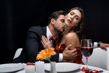 Handsome man kissing beautiful girlfriend during romantic dinner isolated on black