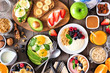 Healthy breakfast table scene with fruit, yogurts, smoothie bowl, oatmeal, nutritious toasts and egg skillet. Above view over a wood background.