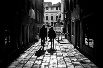 Sticker - Grayscale shot of two men walking down an alley casting shadows on the foreground