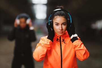 Two young fitness woman with headphones ready for jogging under overpasses during a cold day