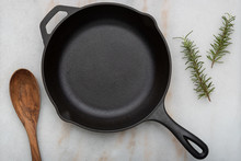 Cast Iron Frying Pan With Spoon On White Background With Rosemary Sprigs