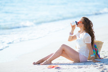 Young Woman Drinking Coffee While Sitting On Beach