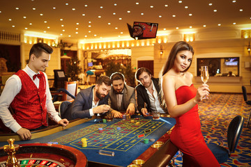 A woman with glass of champagne in a dress at table roulette in casino.