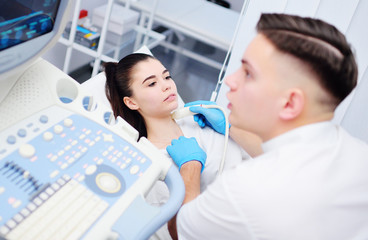 a young male doctor makes an ultrasound of the thyroid gland to a female patient.