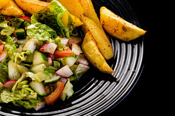 fresh vegetable salad and perfectly fireproof potato on black plate, black background