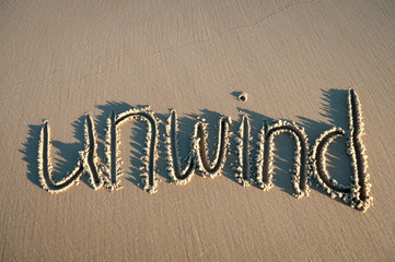 Unwind message handwritten in pristine brown sand with sun and shadows