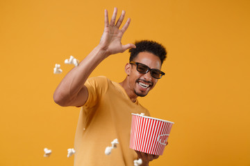 Sticker - Cheerful young african american guy in 3d imax glasses posing isolated on yellow orange background. People lifestyle concept. Mock up copy space. Watching movie film, holding bucket, throwing popcorn.