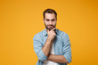 Attractive young bearded man in casual blue shirt posing isolated on yellow orange background studio portrait. People sincere emotions lifestyle concept. Mock up copy space. Put hand prop up on chin.