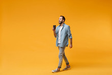 Cheerful Young Man In Casual Blue Shirt Posing Isolated On Yellow Orange Background, Studio Portrait. People Sincere Emotions Lifestyle Concept. Mock Up Copy Space. Hold Paper Cup Of Coffee Or Tea.