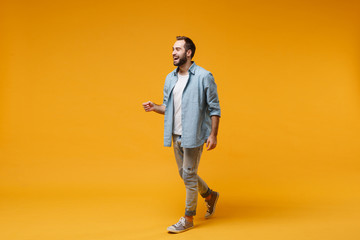 Wall Mural - Cheerful laughing young bearded man in casual blue shirt posing isolated on yellow orange wall background studio portrait. People sincere emotions lifestyle concept. Mock up copy space. Looking aside.