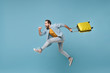 Side view of funny traveler tourist man in yellow clothes isolated on blue background. Male passenger traveling abroad on weekends. Air flight journey concept. Jumping like running, hold suitcase.