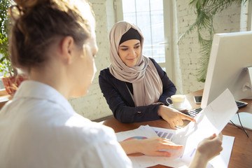 Wall Mural - Reviewing docs with colleague. Beautiful arabian businesswoman wearing hijab while working at openspace or office. Concept of occupation, freedom in business area, leadership, success, modern solution