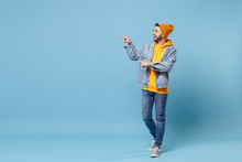 Excited Young Hipster Guy In Fashion Jeans Denim Clothes Posing Isolated On Pastel Blue Background Studio Portrait. People Emotions Lifestyle Concept. Mock Up Copy Space. Pointing Index Fingers Aside.