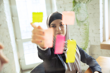 Wall Mural - Organizing tasks. Portrait of a beautiful arabian businesswoman wearing hijab while working at openspace or office. Concept of occupation, freedom in business area, leadership, success, modern