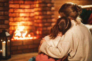 Wall Mural - family mother and child reading book and drink tea on winter evening by fireplace