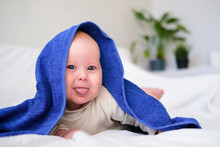 Cute Smiling Caucasian Infant Baby Looking At Camera In Blue Towel After Bathing In The Bath On White Bed. Copyspace
