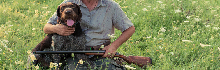 A man with a gun in his hands and an green vest on a pheasant hunt in a wooded area in cloudy weather. Hunter with dogs in search of game.