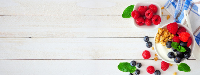 Wall Mural - Healthy yogurt with fresh blueberries and raspberries. Banner with side border against a white wood background. Copy space.