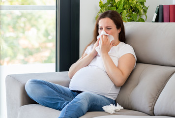 ill pregnant woman coughing sitting on a couch