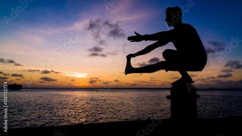 Fotomural Silhouette Man Exercising On Bollard By Sea During Sunset