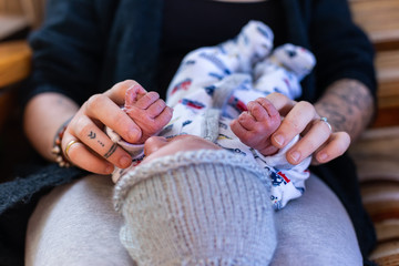 Wall Mural - A selective focus abstract view of a mother and newborn infant at home. Baby boy grabs fingers of modern parent with tattooed arms. Copy space to sides