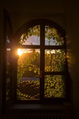 Poster - Vertical shot of an opened arched window with the sun shining in the background