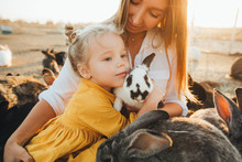 Mom And Daughter Visit A Petting Zoo With Rabbits On The Eve Of Easter. Holiday, Easter Traditions.