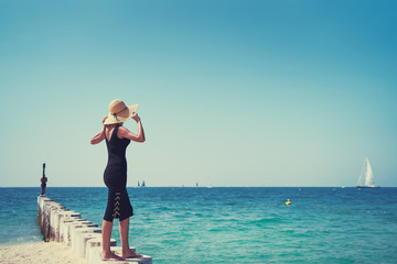 Poster - Lonely and calm. Vacation on the sea. Young woman in hat walking  on beach.