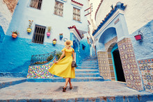Colorful Traveling By Morocco. Young Woman In Yellow Dress Walking In  Medina Of  Blue City Chefchaouen.