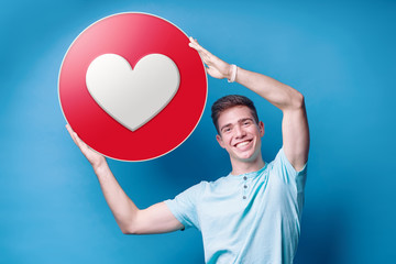 Colorful studio portrait of young man holding love empathetic emoji reaction, printed on paper.