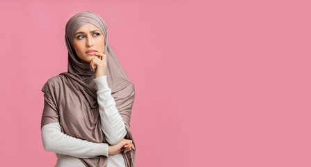 Wall Mural - Pensive muslim girl thinking and looking away on pink studio background